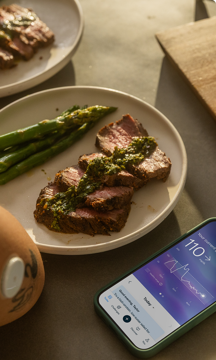 A plate of steak and asparagus next to a phone showing glucose data